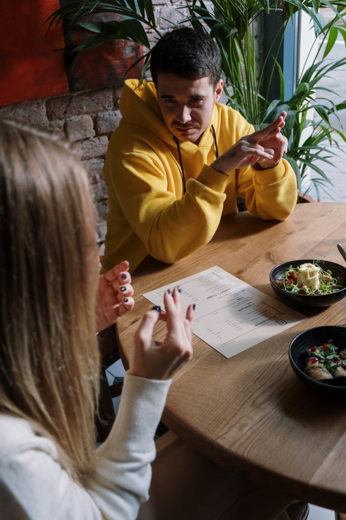 Two friends communicate using sign language at a restaurant table with salads.
