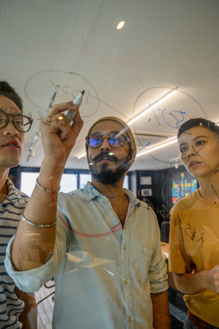 Three colleagues brainstorming on a glass board during a creative office meeting session.